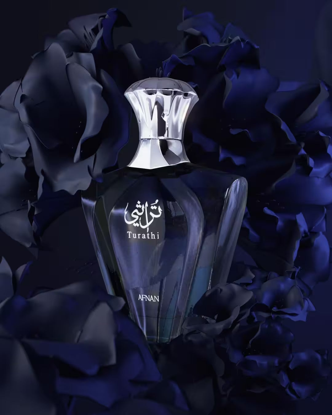 A dark glass perfume bottle with a faceted silver cap, labeled 'Tarathi' and 'AFNAN', centered among deep navy blue rose petals on a dark background.