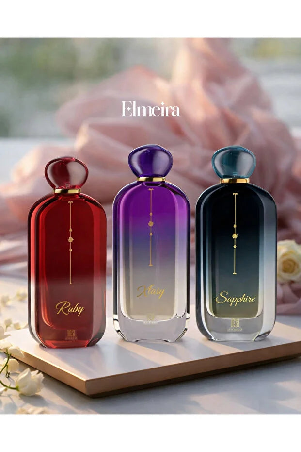 Three Elmeira perfume bottles labeled Ruby, Ruby, and Sapphire on a wooden stand with a blurred background.